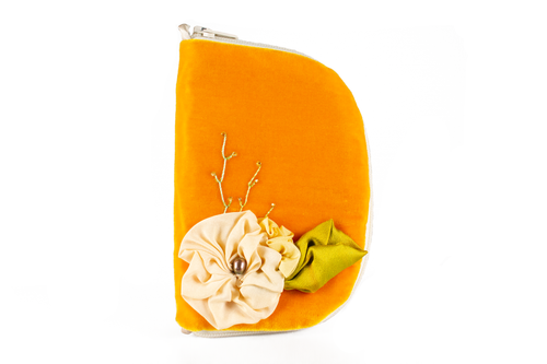 Front view of bright orange velvet jewelry/needle case with cream colored zipper. On the needle case is a cream colored silk flower with one big green leaf and beaded embroidery which looks like vines. The flower has a grey Freshwater pearl sewn into the center. There are two small cream colored loops, one on top and one on bottom.