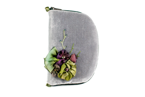 Front view of slate grey velvet jewelry/sewing case featuring a silk floral arrangement of green and purple flowers with beaded vines. Each flower has a freshwater pearl in the center. The zipper is dark green. There are two green loops, one situated at the top and one at the bottom. 