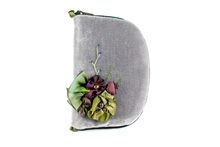 Load image into Gallery viewer, Front view of slate grey velvet jewelry/sewing case featuring a silk floral arrangement of green and purple flowers with beaded vines. Each flower has a freshwater pearl in the center. The zipper is dark green. There are two green loops, one situated at the top and one at the bottom. 

