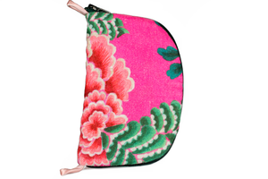 Front view of bright pink floral linen jewelry case with a dark green zipper and two small light pink loops, one situated at the top and one at the bottom. 