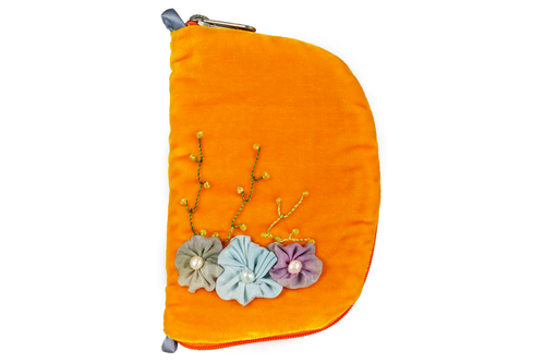 Front view of orange velvet jewelry/sewing case showing a silk flower arrangement. A light blue flower is in the middle, a light purple flower on the right, and a light green flower on the left. Three beaded vines sprawl upwards from the flowers. The zipper is dark orange and dusty blue loops. 